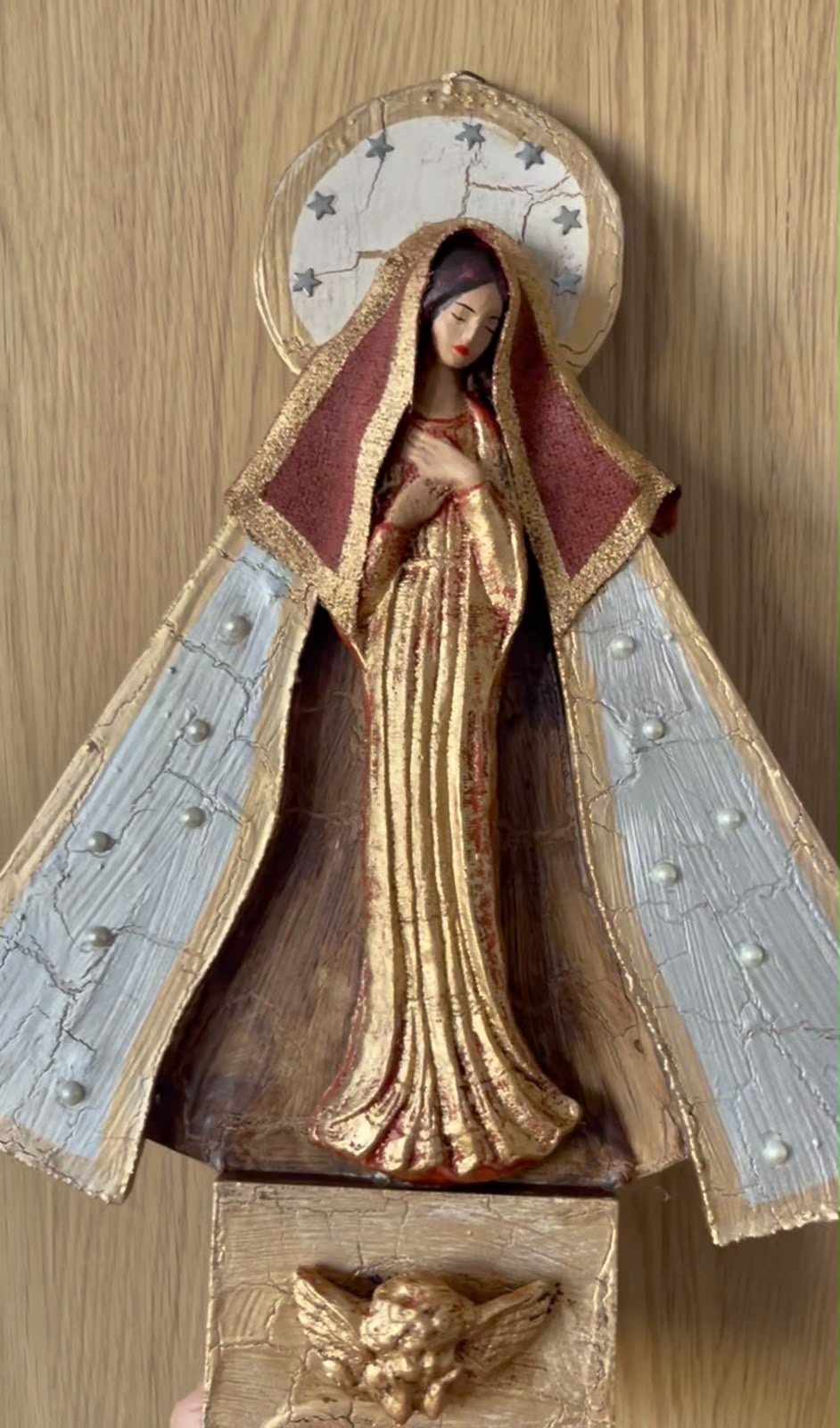 Virgen de madera con manto pintado a mano, colgada sobre un muro de madera